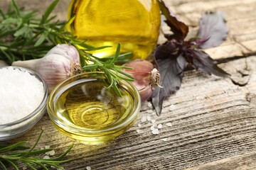 Wall Mural - Cooking oil in bowl, salt, garlic and rosemary on wooden table, closeup