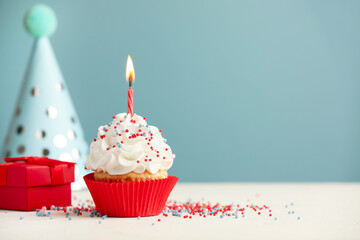 Birthday cupcake with burning candle, gift and party cone on white table. Space for text