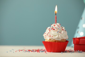 Birthday cupcake with burning candle, gift and party cone on white table. Space for text