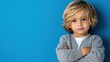 © Pinklife - A confident young boy with blonde hair and a gray sweater poses against a bright blue background, embodying innocence and charm in a vivid, colorful setting.