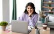 © Prostock-studio - Portrait of smiling laughing young woman sitting at table, wearing wireless headset and using laptop. Young female watching video, movie or webinar, having video call with friends or family