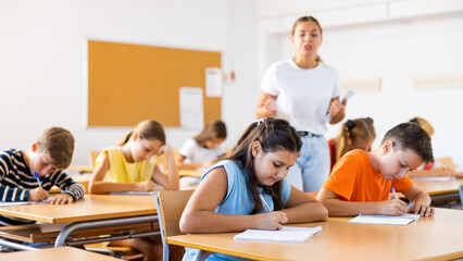 Wall Mural - Group of school kids with pens and notebooks studying in classroom with teacher