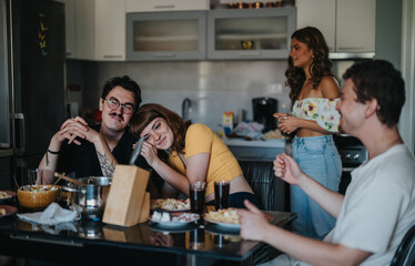 Wall Mural - A group of friends shares a casual dinner, enjoying each other's company with laughter and conversation in a cozy kitchen setting.