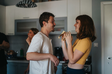 Wall Mural - A cheerful young couple shares a light-hearted moment in a contemporary kitchen, showcasing warmth and joy. The scene captures friendship and a relaxed lifestyle in a home environment.