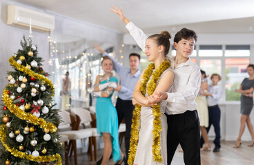 Positive teenage students in festive attire rehearsing ballroom dance number for upcoming Christmas party at college with interested female teacher in background..