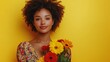 © pongtap - Woman holding vibrant flowers against a cheerful yellow background.