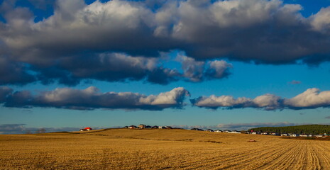 Autumn landscape with a field with mown crops, clouds and a blue sky at sunset