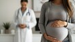 © Cheewynn - Close-up of a pregnant woman holding her belly at a prenatal appointment, blurred doctor in the background, healthcare and motherhood, pregnant woman, prenatal care