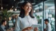 © Phoophinyo - A successful Asian businesswoman standing in her startup's office, surrounded by creative team members, holding a tablet and smiling as she oversees the development of a new product
