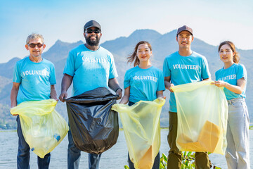 multiethnic people in blue volunteer T-shirt volunteers holding waste sorting plastic bag standing by the river,a diverse group of volunteers join together to cleanup the sand beach together