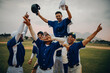 © Jacob Lund - Baseball team celebrating victory on the field, lifting player in a triumphant success