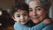 © Lion - Minimalistic stock photo of a grandmother with gray hair holding her young grandson, the boy has dark curly hair, both smiling warmly, indoor setting with soft natural light