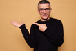© sementsova321 - Cheerful man wearing raglan pointing aside with toothy smile and raised arm showing joy and satisfaction feeling happy directing attention to empty space isolated over beige background