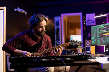 Leinwandbilder - Young singer recording new acoustic guitar accords in home studio, creating a new song and editing on daw software interface on pc. Songwriter composing soundtracks with amplifier tool.
