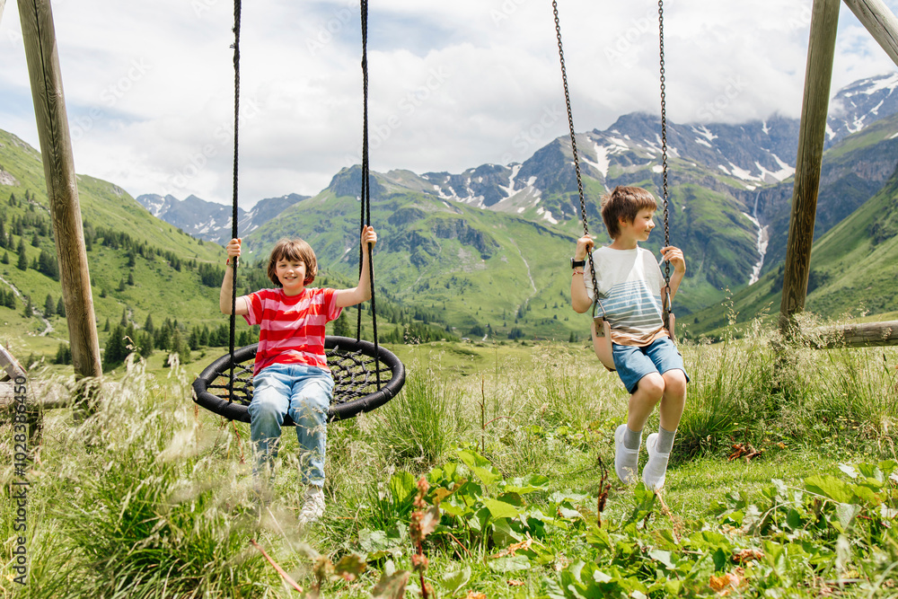 Brother and sister sitting on swing at meadow Stock Photo | Adobe Stock