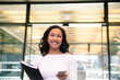 © Westend61 - Smiling businesswoman holding documents and smart phone in office