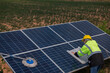 © VIEWFOTO STUDIO - Service worker in PPE. cleaning  with solar panel with wind turbine on background.