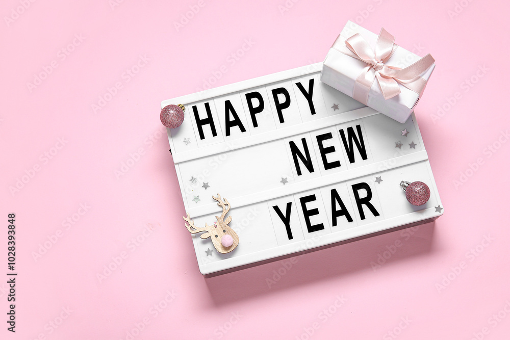 Board with text HAPPY NEW YEAR, gift box and Christmas decorations on pink background