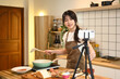 © Prathankarnpap - Smiling young woman holding spatula, recording cooking video in her home kitchen