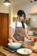 © Prathankarnpap - Attractive young asian housewife wearing apron preparing breakfast in the kitchen