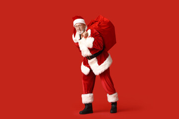 Santa Claus with bag full of gift boxes on red background