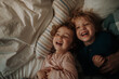 © Halfpoint - Candid portrait of siblings lying together in bed, looking at the camera and laughing. Top view.