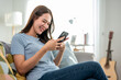 © Kawee - Asian beautiful woman sitting on sofa and using mobile phone in house.