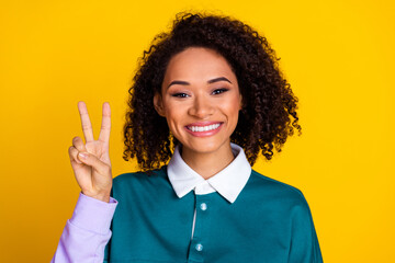 Poster - Portrait of good mood cute positive girl with wavy hairstyle wear teal shirt showing v-sign symbol isolated on yellow color background