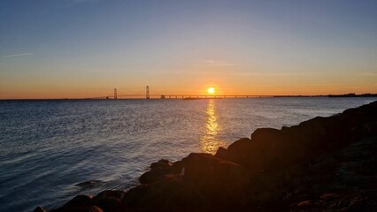 Poster - Sunset over the sea with a bridge in the distance.