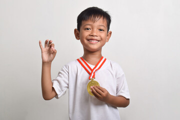 Little asian boy wearing a gold medal of an award competition. Smiling child celebrating his success, isolated on a white background with an okay sign with fingers, excellent symbol