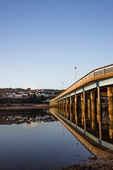 Scenic view of a bridge reflecting in calm water with a clear blue sky and a town in the background