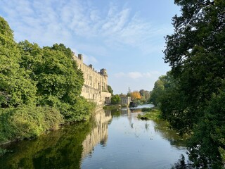 Historic castle beside a river with lush greenery and blue sky.