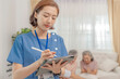 © ultramansk - A healthcare professional uses a tablet to update medical records while elderly individuals sit in the background, indicating a supportive healthcare environment that focuses on senior care.