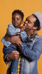 Wall Mural - Vertical Video African american young dad hugging his sweet little son and playing with him, making the baby boy laugh and bonding together. Joyful family enjoying leisure time with each other. Camera