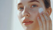 © AGCreative - young woman with flawless skin applies skincare product to her face, showcasing fresh and radiant look. Her expression reflects confidence and care for her skin