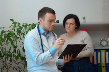 A young doctor, at his workplace, receives patients. He examines a woman, measures saturation, pulse.