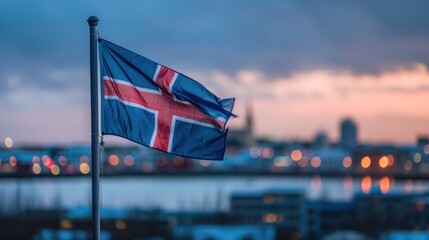 Icelandic flag waving against blurred cityscape at sunset