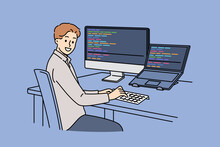 Man programmer types code and looks at camera, sitting at table with computer and laptop. Successful guy programmer develops software or application, working in team with UI or UX designers