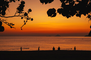 silhouettes of people relaxing on beach by sea in the morning at sunrise in summer