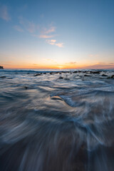 Wall Mural - peaceful sunrise over a rocky beach shore.