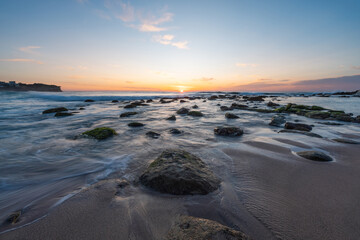 Wall Mural - beautiful sunrise over a rocky beach shore.