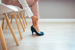 © Dragana Gordic - Woman Adjusting High Heel Shoes in Modern Office Setting