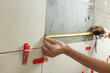 © triocean - Woman tiling bathroom walls, using tape measure for measuring length. Process of installation of tiles in the bathroom step by step. DIY home improvement.