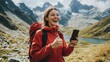 © Uliana - An excited woman in a picturesque mountain setting, holding her smartphone and grinning widely, celebrating the completion of a challenging hike with friends.