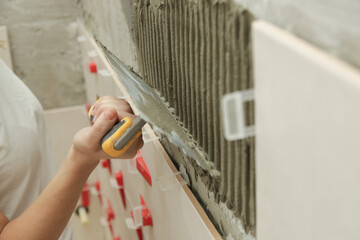 Woman tiling bathroom walls, applying adhesive on a tile and placing ceramic tile in right position. Process of installation of tiles in the bathroom step by step. DIY home improvement.	