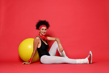 Wall Mural - Aerobics. Happy woman with fitness ball on red background