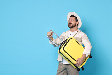 Canvas Print - Happy man with suitcase on light blue background, space for text