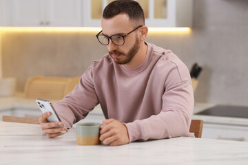 Poster - Handsome man using smartphone at white table in kitchen