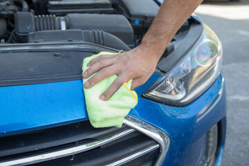 A man is wiping a car with a cloth.