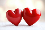 Two glossy red hearts placed closely on a soft surface, symbolizing love and affection